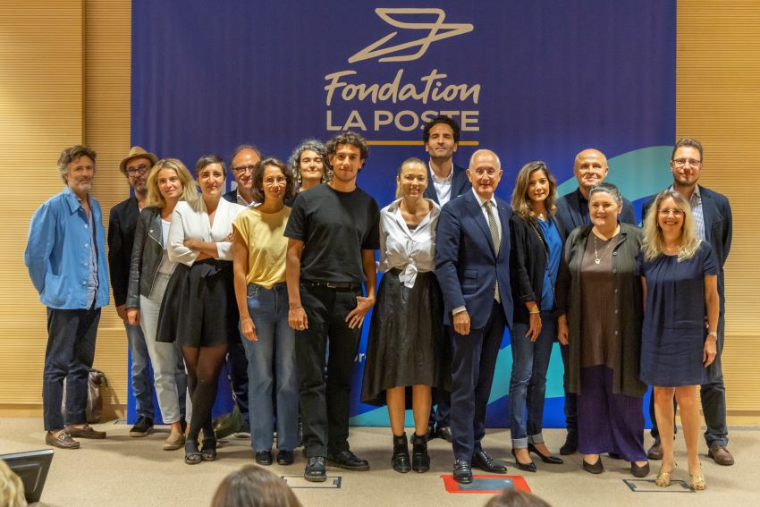 Photo de groupe sur scène : membres du jury, anciens  lauréats du prix, éditeurs, nouveau lauréat, président de La Poste, déléguée générale de la Fondation...