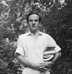 Photo en noir et blanc de François Truffaut, de face, portant des livres sous le bras