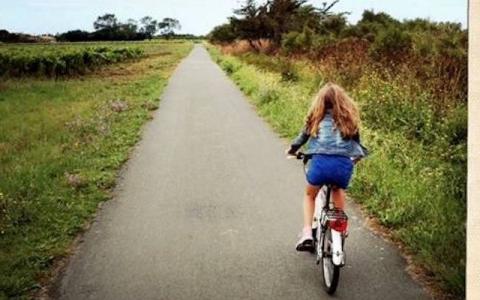 Photo d'une petite fille de dos à vélo sur une route de campagne